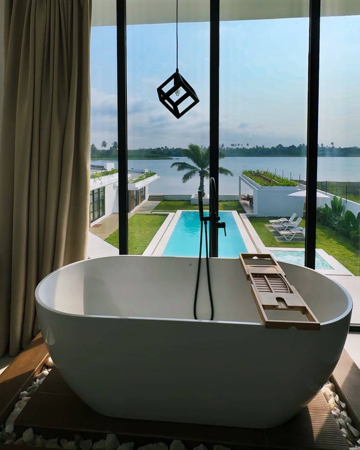 Freestanding jacuzzi framed by full-height windows over the pool and water