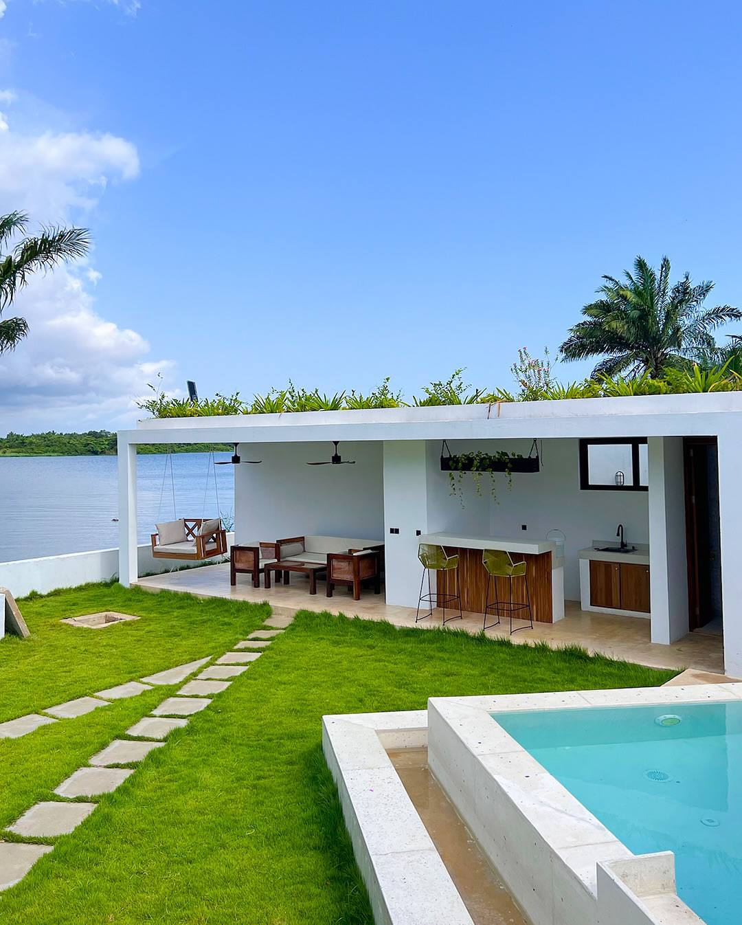 Open waterside pavilion with swing seat, lounge and lawn path beside the pool